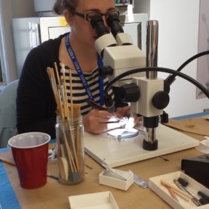 Conservator looking through a microscope to remove corrosion on an artifact