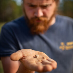 Archaeological Field Technician Josh Barber examines the lead die found in one of the mud and stud post molds in the burial excavation area.