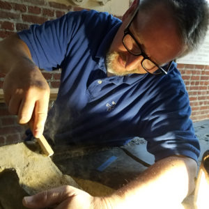 Conservator using a brush to clean the edges of a tombstone