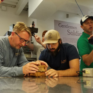 Two men examine a small metal box