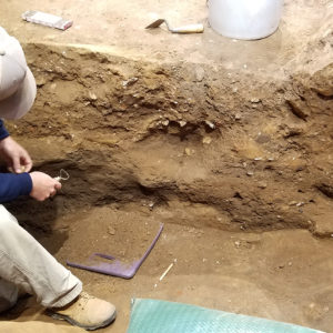 Archaeologist cleans an excavation unit profile