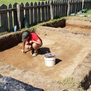 Archaeologist excavates in front of fence