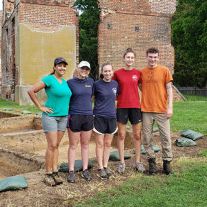 Five archaeologists stand in front of excavations and brick ruins