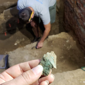 Hand holding copper scrap with excavating archaeologist in background