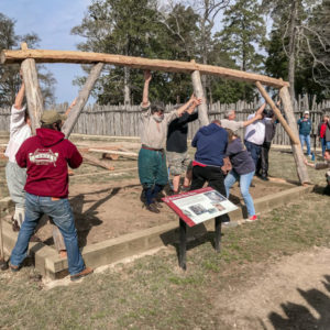 A group of people raising one side of a timber frame onto its foundation