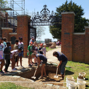 School group watches two archaeologists excavating