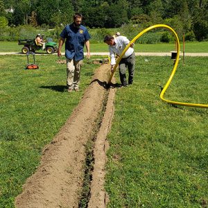 Archaeologist Bob Chartrand and former Director of Archaeology David Givens help install conduit for fiber optic cable in 2019. This summer's excavations at the cellar daylighted the conduit once again.