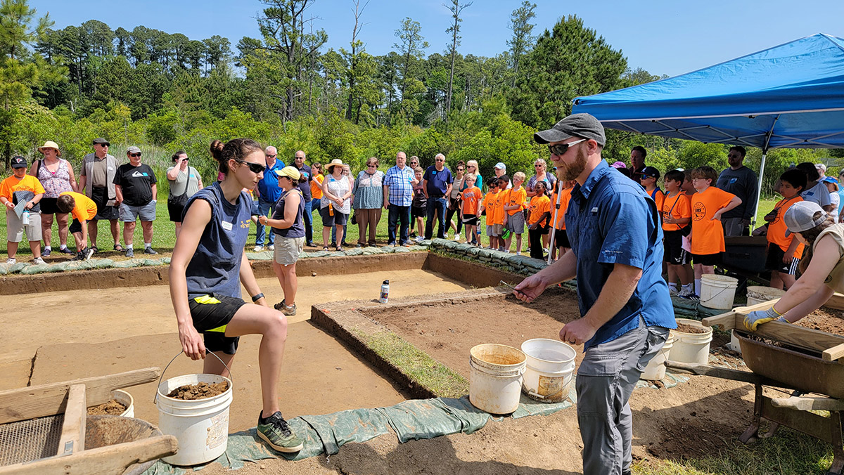 Visitors on the archaeology tour listen as archaeologist Hannah Barch explains the north field excavations.