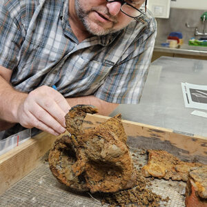 Archaeological Conservator Dr. Chris Wilkins removes soil concretions from one of the sword hilts found in the Governor's Well.