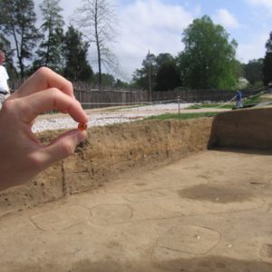 Hand holding small bead with excavation unit in the background