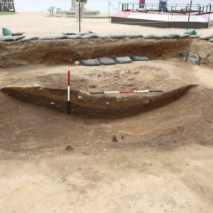 Measuring sticks laid horizontally and vertically next to stratigraphic layers within an excavation unit lined with sandbags