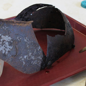 solution being painted onto a corroded close helmet propped on an empty bottle on a tray