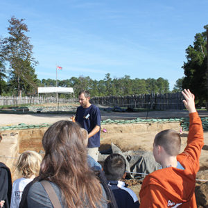 Archaeologist speaking to a school tour as child raises their hand to ask a question