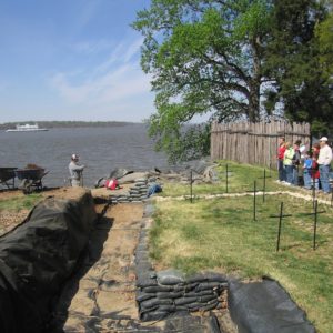 Archaeologists talking to visitors with grave markers and sandbags in foreground