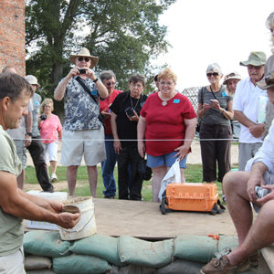 An archaeologist shows an excavated glass vessel to additional staff members and visitors