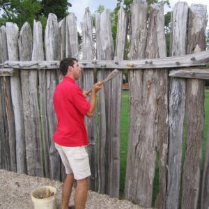 Man hammering a peg into a crosspiece of a wooden palisade