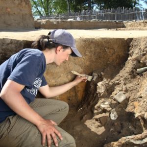 Archaeologist brushing artifacts in an excavation unit wall