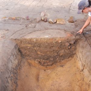 Archaeologist pointing to a bisected ditch showing various stratigraphic layers in the profile