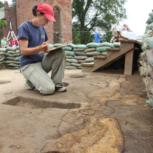 archaeologist recording features in an excavation area lined with sandbags