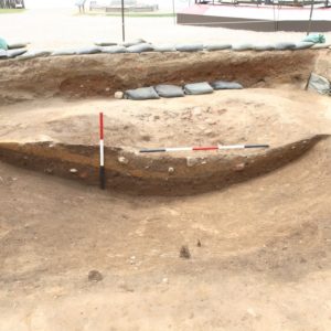 Measuring sticks laid horizontally and vertically next to stratigraphic layers within an excavation unit lined with sandbags