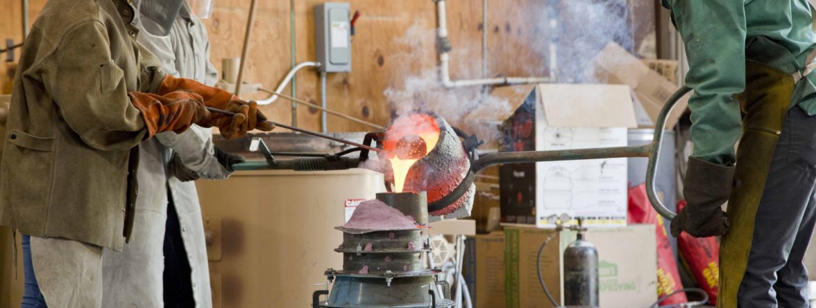 workers in protective gear pouring molten bronze into a mold