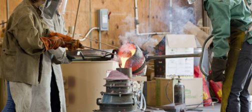 workers in protective gear pouring molten bronze into a mold