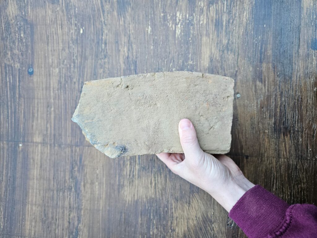 A muddy brick that is rounded on one side with one short edge that is no longer at a 90-degree angle.