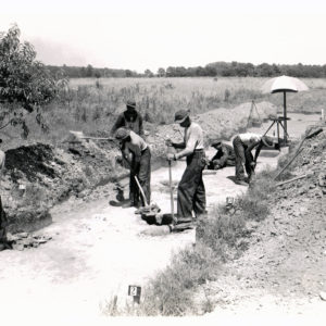 Black and white photograph of excavators working along a road