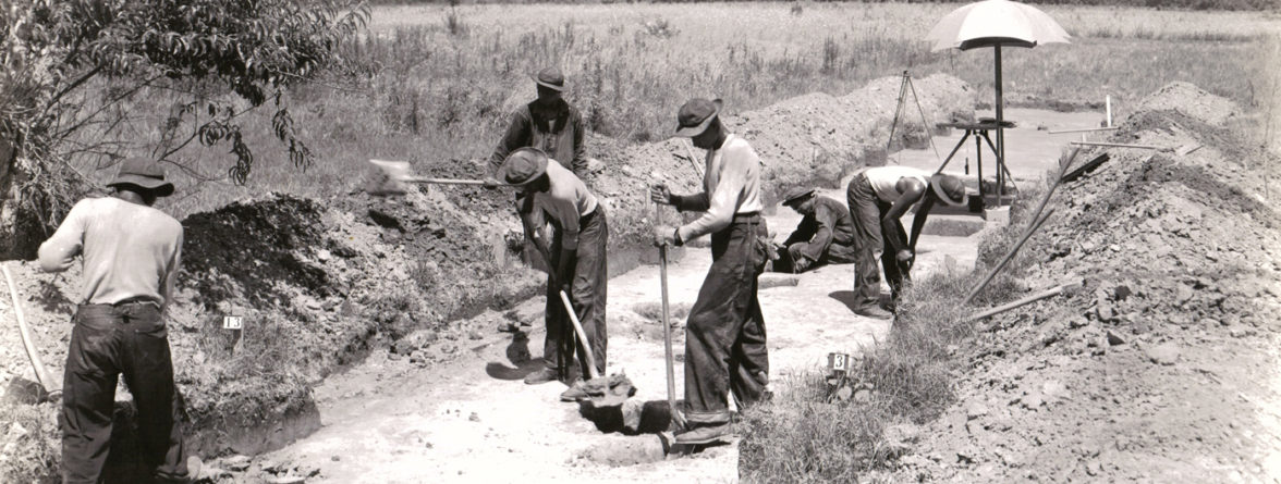 Black and white photograph of excavators working along a road