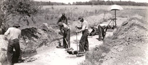 Black and white photograph of excavators working along a road