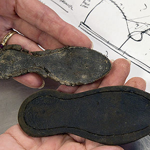 hands holding two leather shoes in front of measured drawing