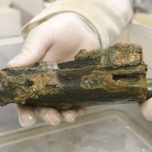 Gloved hands holding a corroded pistol over a plastic tub