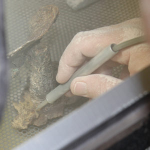 Air abrasion tool being used to clean a small flask