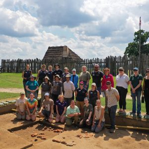 Field school students and archaeology and collections staffs take a group shot at the cellar excavations. James Fort is in the rear.