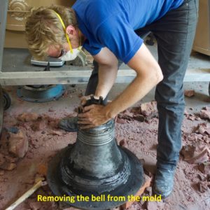 Worker removes cast bell from mold