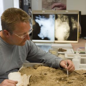 Conservator using a pick to remove corrosion from a jack of plates