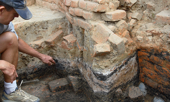 Archaeologist pointing to ash layer in unit wall