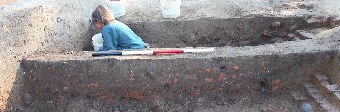 Archaeologist excavating on other side of unit wall