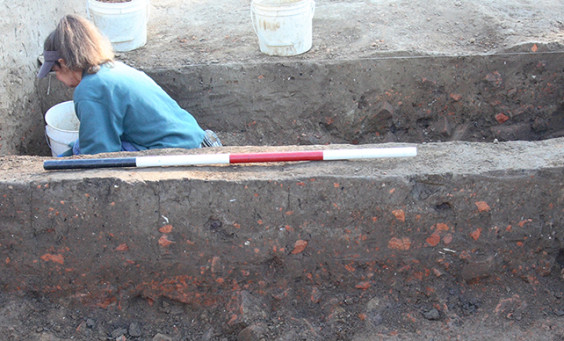 Archaeologist excavating on other side of unit wall