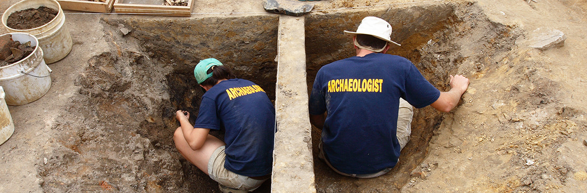 two archaeologists excavate on either side of a balk in the middle of a unit