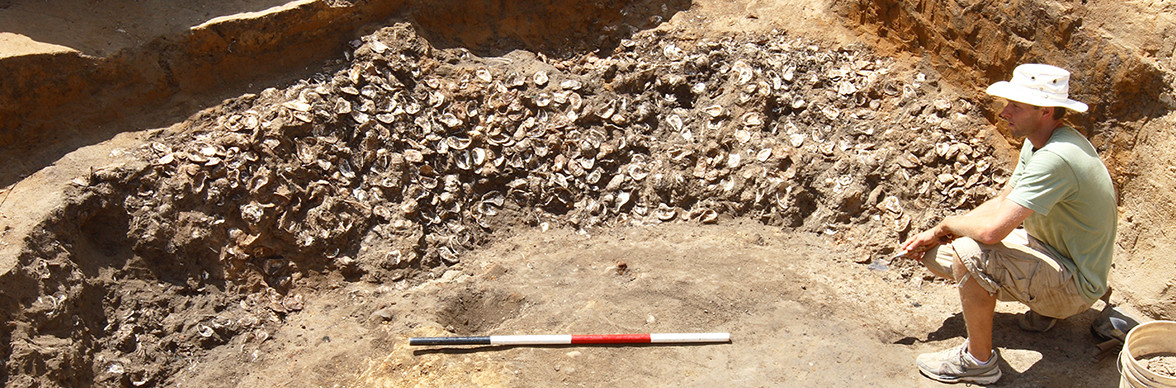 archaeologist sits next to a large pile of oyster shells