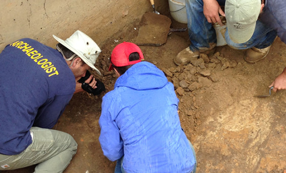 Archaeologist video recording excavations while others trowel nearby