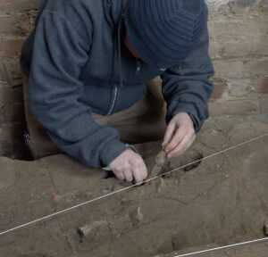 Staff Archaeologist Caitlin Delmas excavates an iron knife blade found in the fort's eastern palisade wall within the Church Tower.