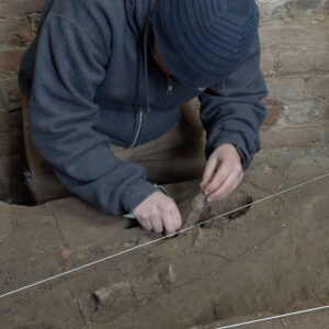 Staff Archaeologist Caitlin Delmas excavates an iron knife blade found in the fort's eastern palisade wall within the Church Tower.