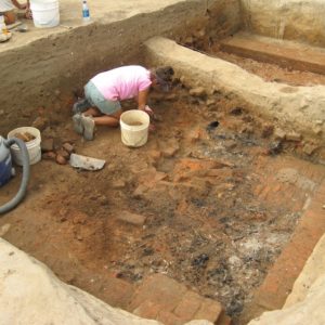 Archaeologist using a trowel to excavate a brick floor