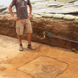 man examining an outlined posthole feature in an excavation unit