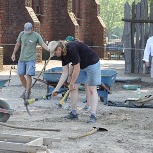 Three excavators working next to an assortment of wheelbarrows and tools in front of a brick church