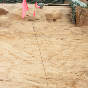 Flags marking a feature within a large excavation area lined with sandbags