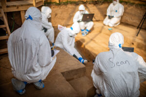 Dr. Ashley McKeown dictates her observations of one of the individuals to the archaeology team prior to his removal to the lab. The team wrote their names on their Tyvek suits so that they're identifiable during the excavations (human remains intentionally obscured).