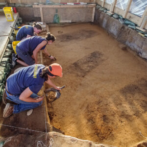 Staff Archaeologist Natalie Reid, Site Supervisor Anna Shackelford, and Senior Staff Archaeologist Mary Ann Hartley excavating inside the burial structure at the 1607 burial ground. The graves are the three dark rectangles.